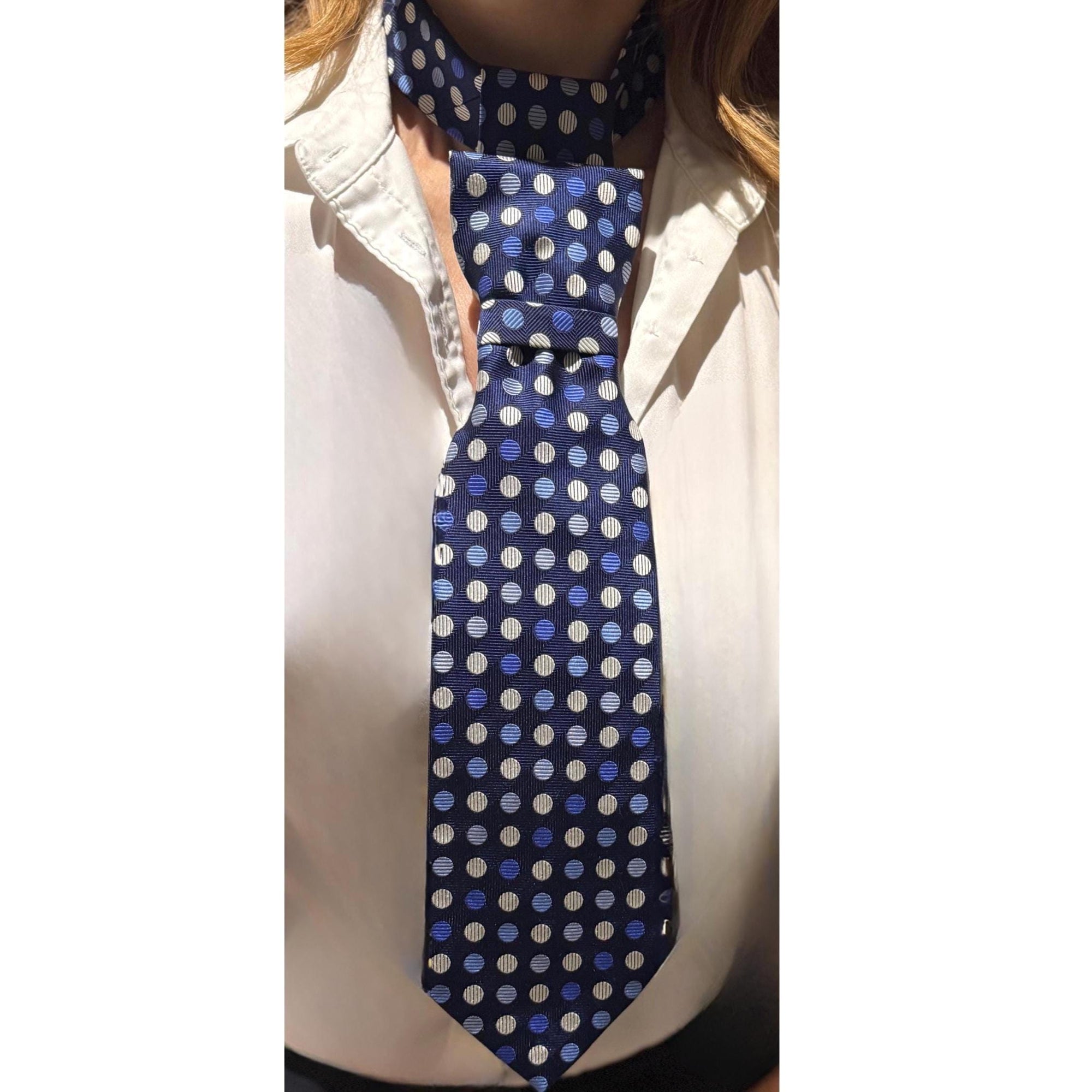 Detailed shot of the adjustable gold clasp on a navy silk polka dot tie, showcasing the traditional English silk weave.