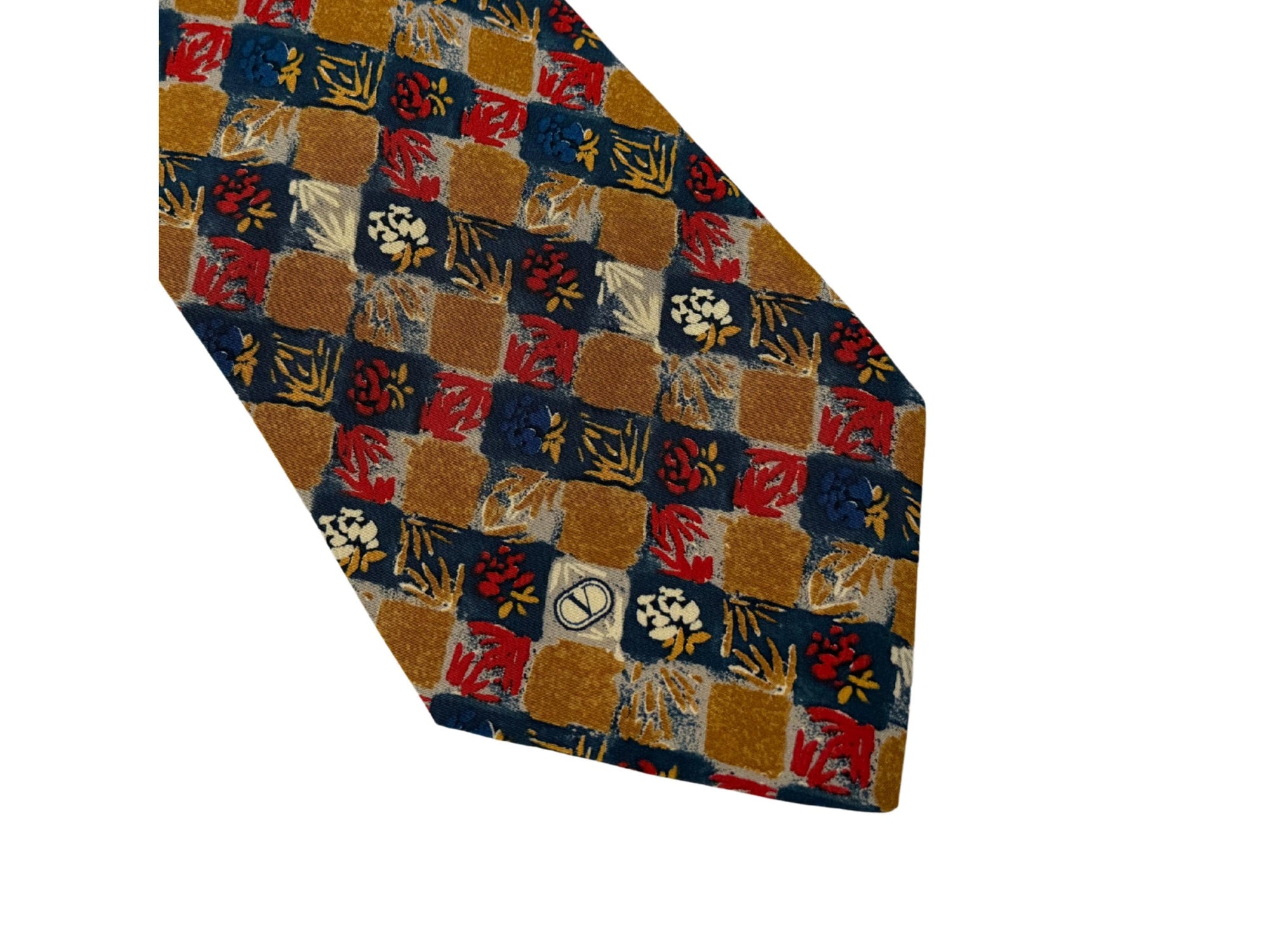 Close-up of a Valentino vintage silk tie in gold, red, and navy geometric floral pattern, showing the signature V logo detail.