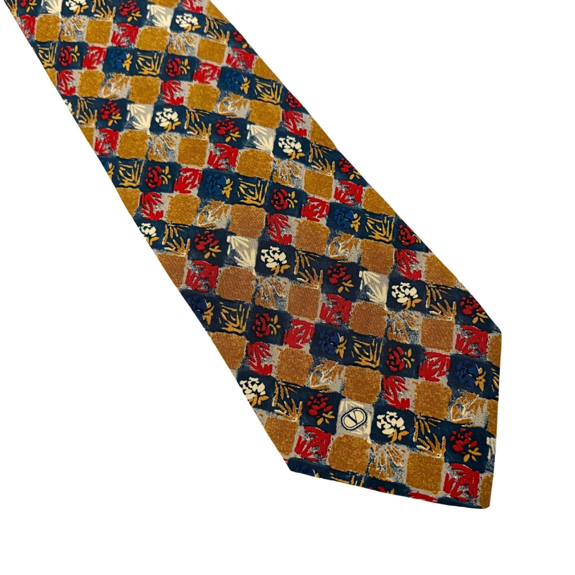 Close-up of a Valentino vintage silk tie in gold, red, and navy geometric floral pattern, showing the signature V logo detail.